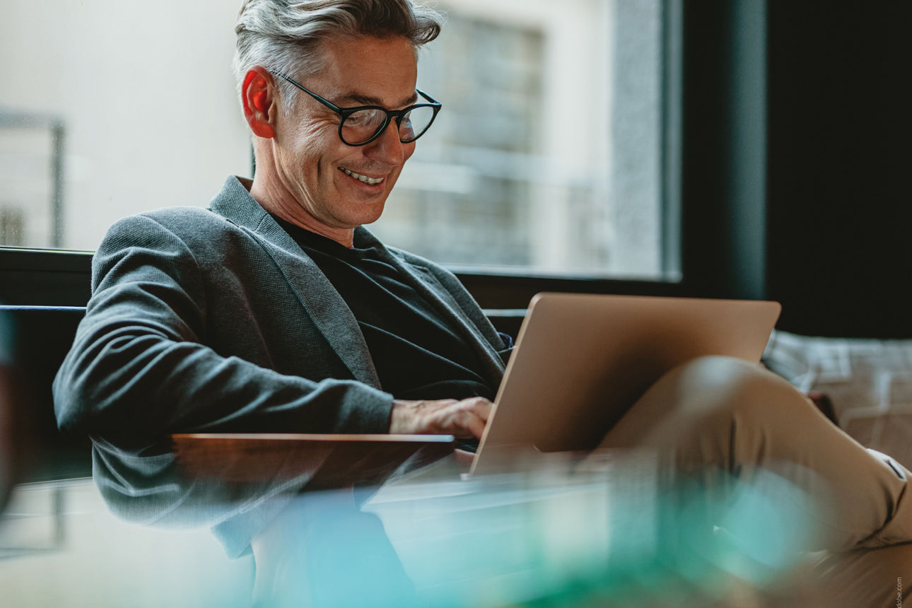 eine Person mit Brille sitzt lächelnd am Laptop