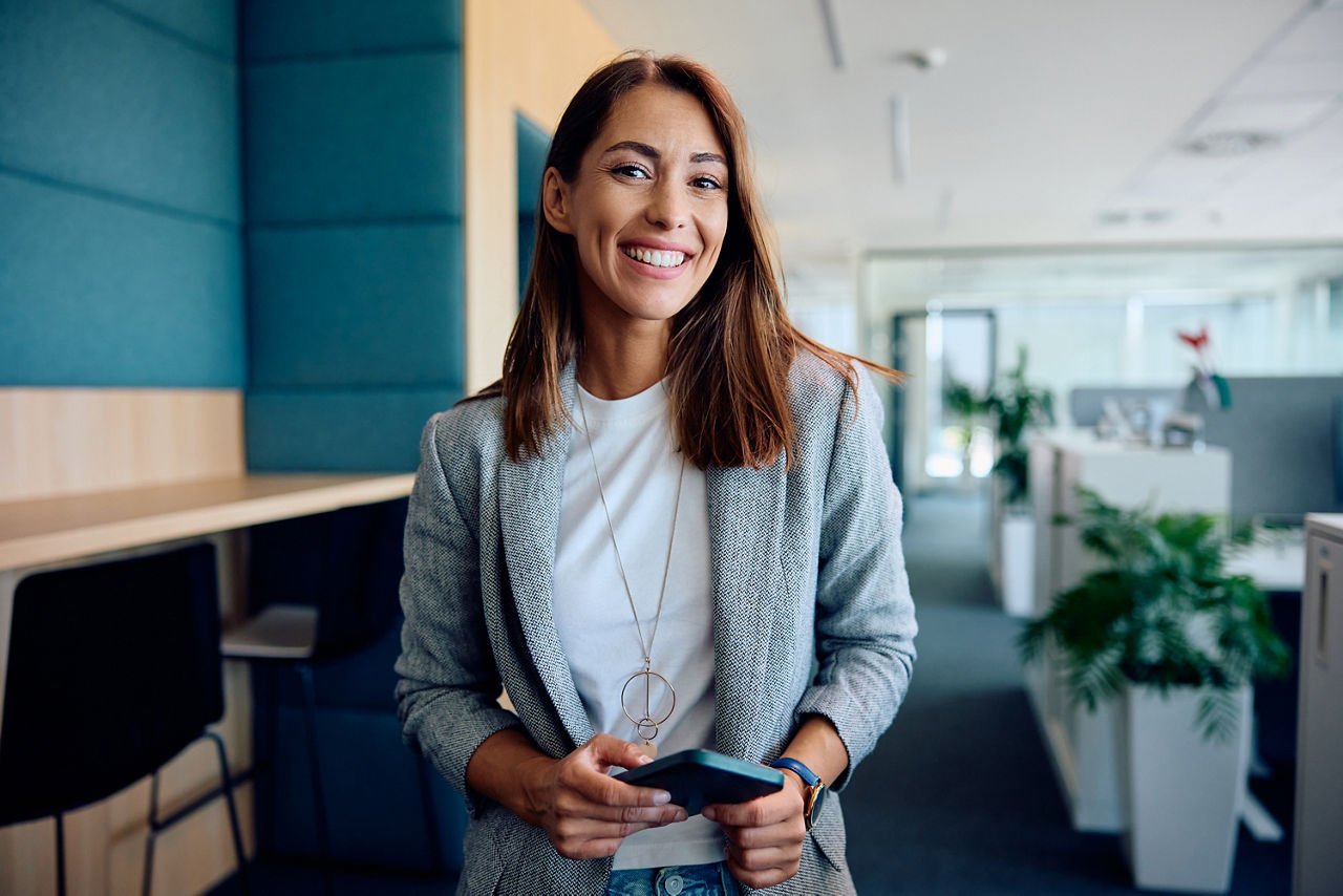 Fröhliche Frau im Büro, lächelt in die Kamera.