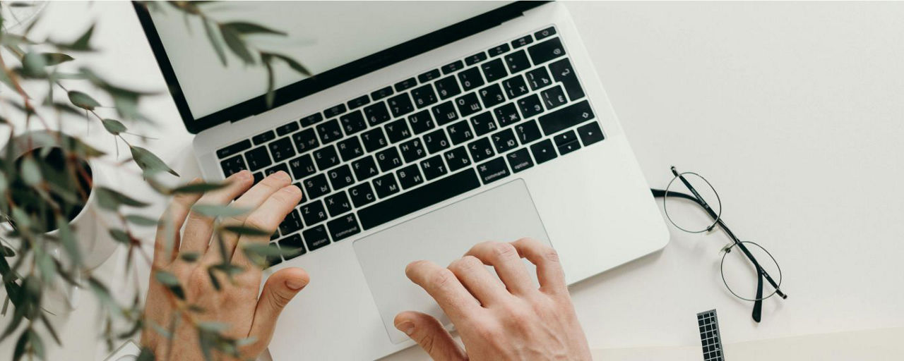 Hände tippen an einem Laptop, daneben liegt eine Brille