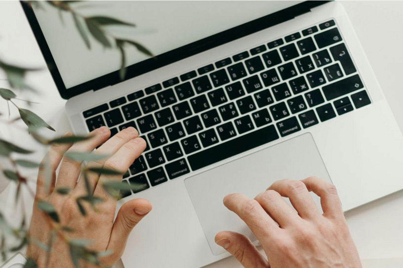 Hände tippen an einem Laptop, daneben liegt eine Brille