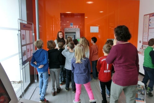 Frau zeigt Kindern die Selbstbedienungsgeräte in der Schalterhalle