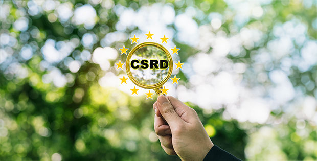 Eine Hand hält ein Vergrößerungsglas mit dem Wort „CSRD“ in der Mitte des Glases.