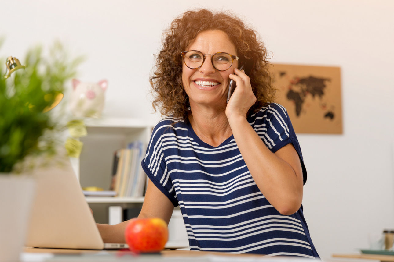 Frau vor einem Laptop telefoniert mit dem Smartphone in der Hand weil sie zurückgerufen wird