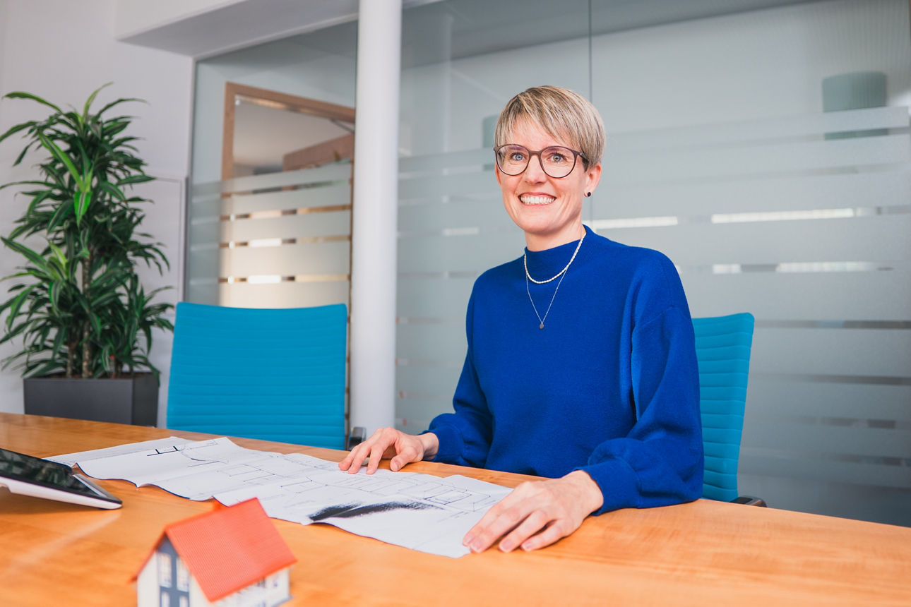 Frau Kuhner sitzt am Tisch mit einem Bauplan und einem Modellhaus