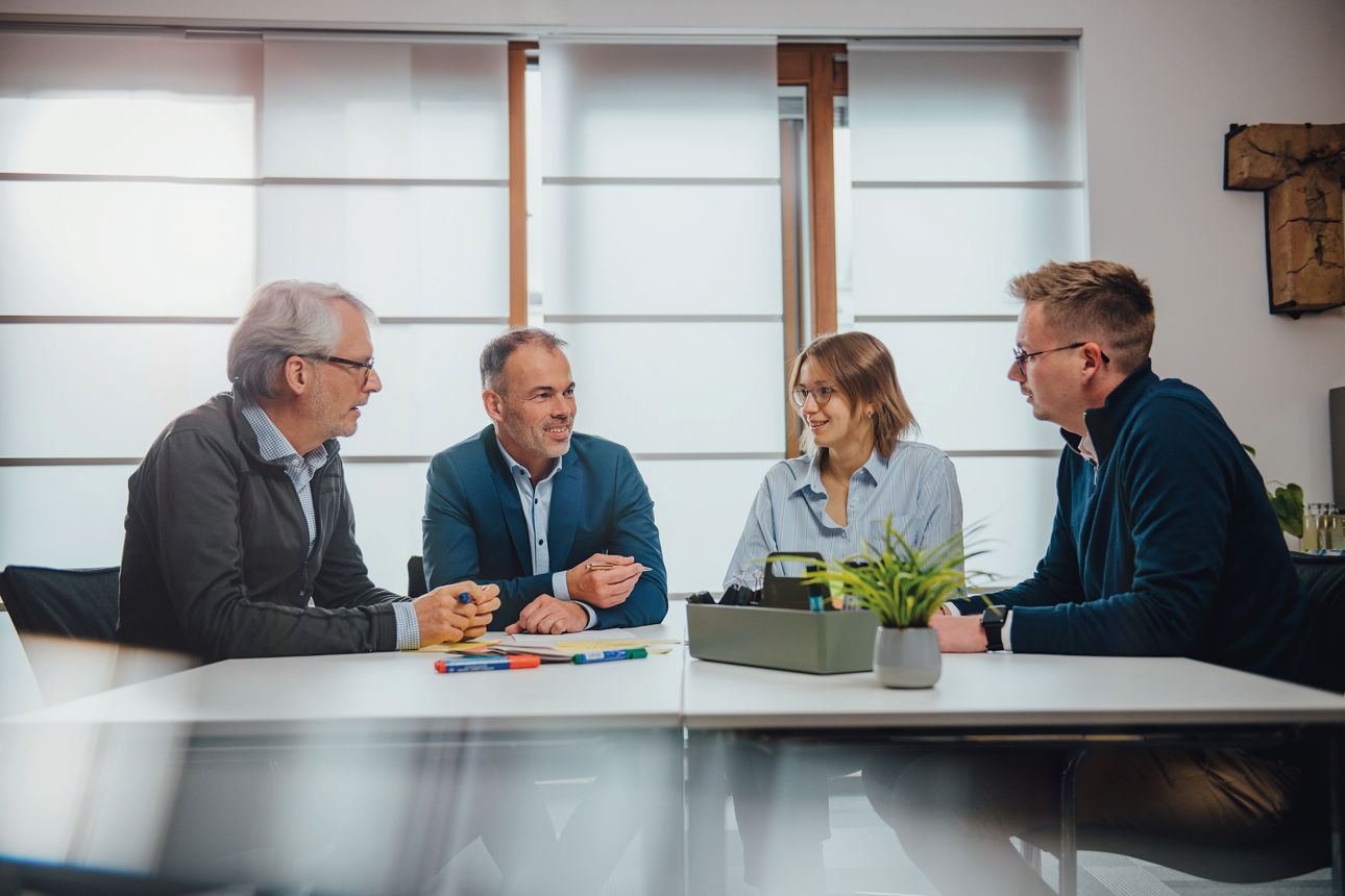 Vier Mitarbeitende sitzen am Tisch und führen ein Gespräch