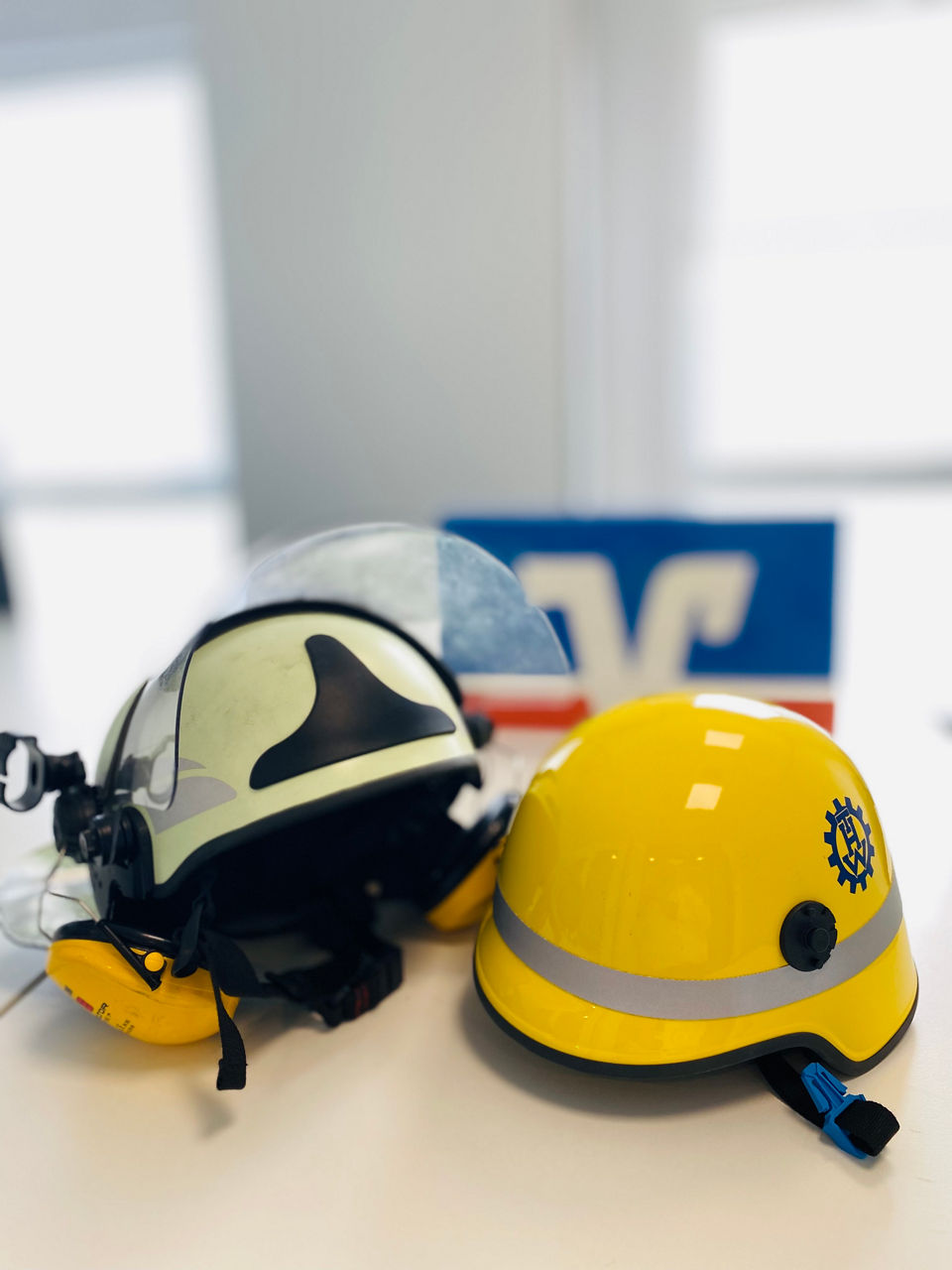 Je ein Helm der Feuerwehr und des Technischen Hilfswerkes liegen auf einem Tisch