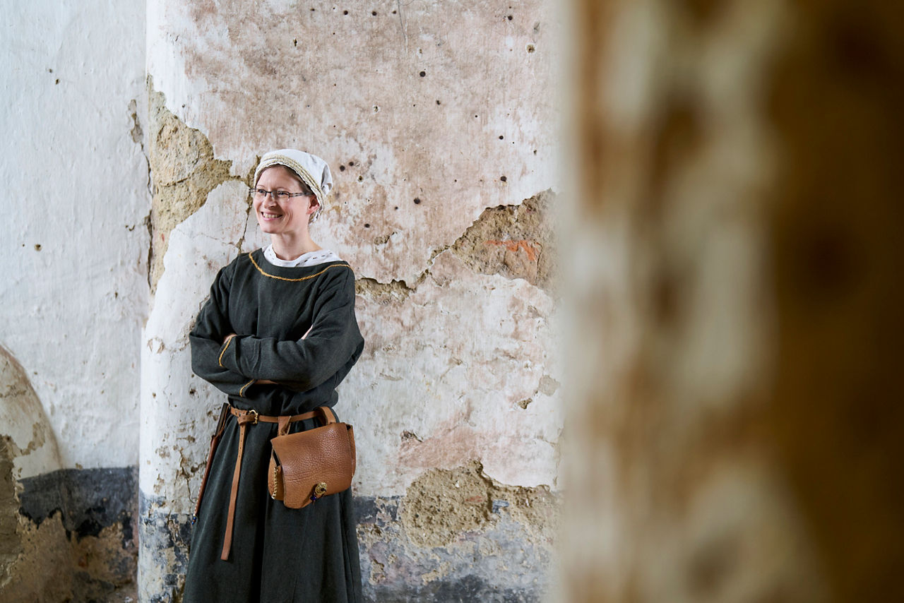 Corinna Seidler in mittelalterlichem Gewand an eine Wand gelehnt
