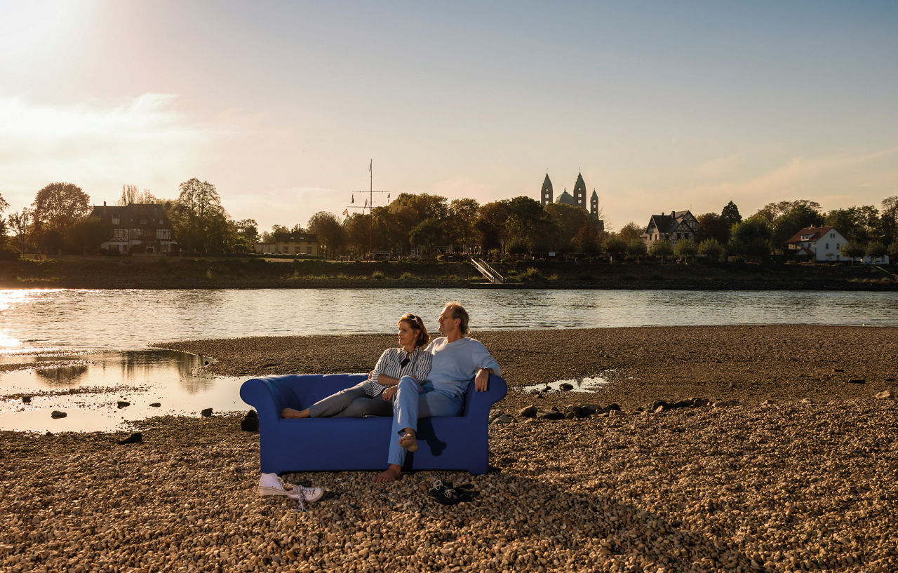 Ehepaar sitzt auf einer Couch die auf einer Kiesbank steht