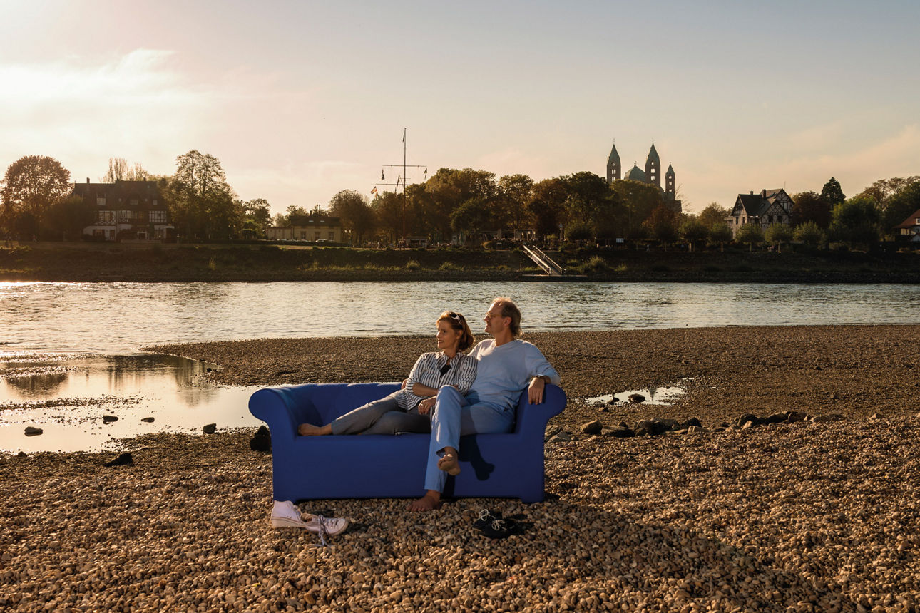 Ehepaar sitzt auf einer Couch die auf einer Kiesbank steht