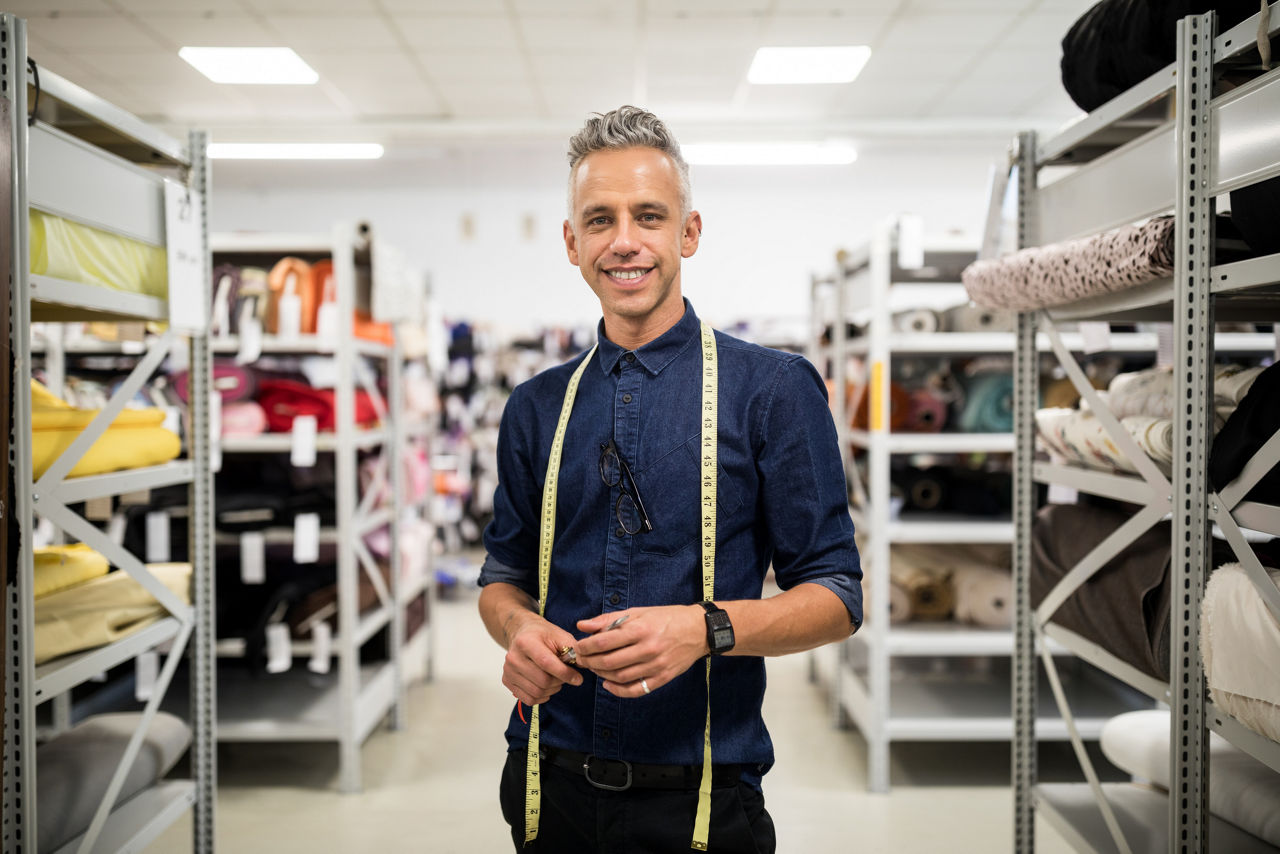 Successful male fabric store owner. Portrait of male fashion designer with tape measure standing in textile store looking at camera confidently.