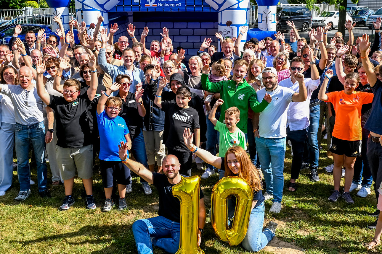 Ein Mann mit einem Luftballon mit der Zahl 1 und eine Frau mit einem Luftballon mit der Zahl 0 vor vielen Leuten.