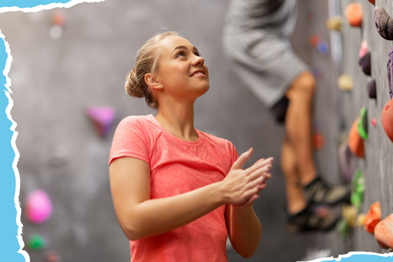 Junge Frau steht vor einer kletterwand und schaut nach oben