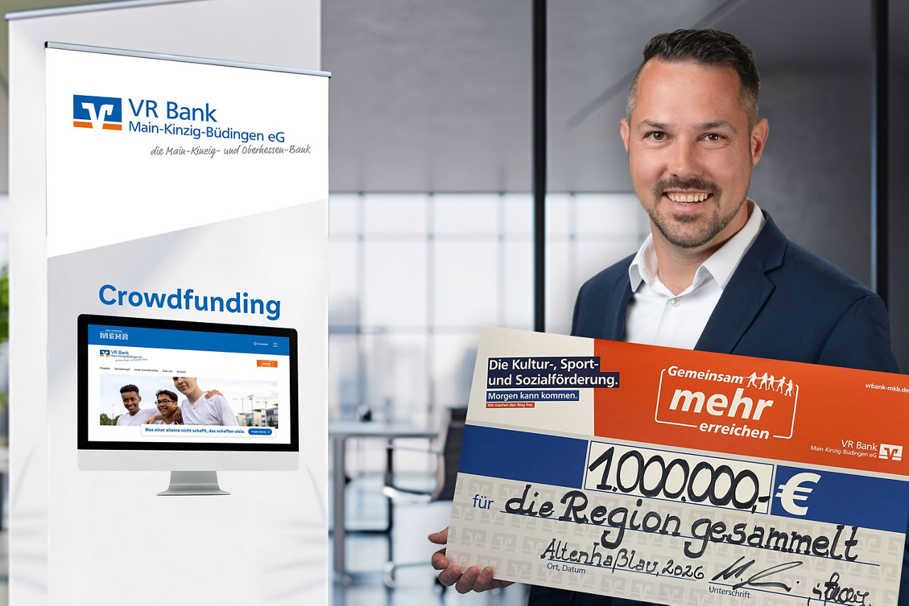 Das Bild zeigt einen Mitarbeiter der VR Bank Main-Kinzig Büdingen mit einem Spendenscheck. Auf dem Scheck ist der Betrag von einer Millionen Euro abgebildet, darunter steth "für die Region gesammelt" im Hintergrund sieht man ein Banner auf dem die Seite der Crowdfunding-Plattform abgebildet ist.