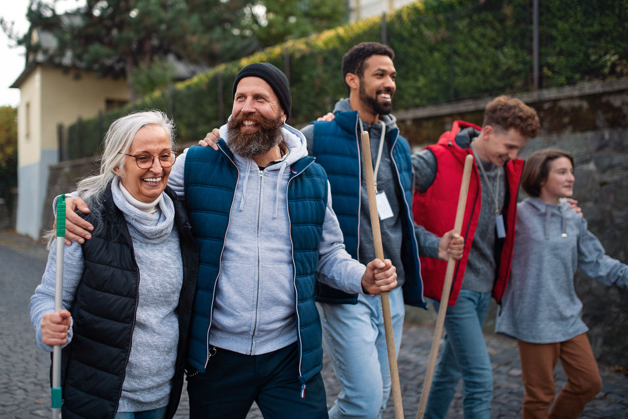 A diverse group of happy volunteers walking with tools to do street clean up, community service concept