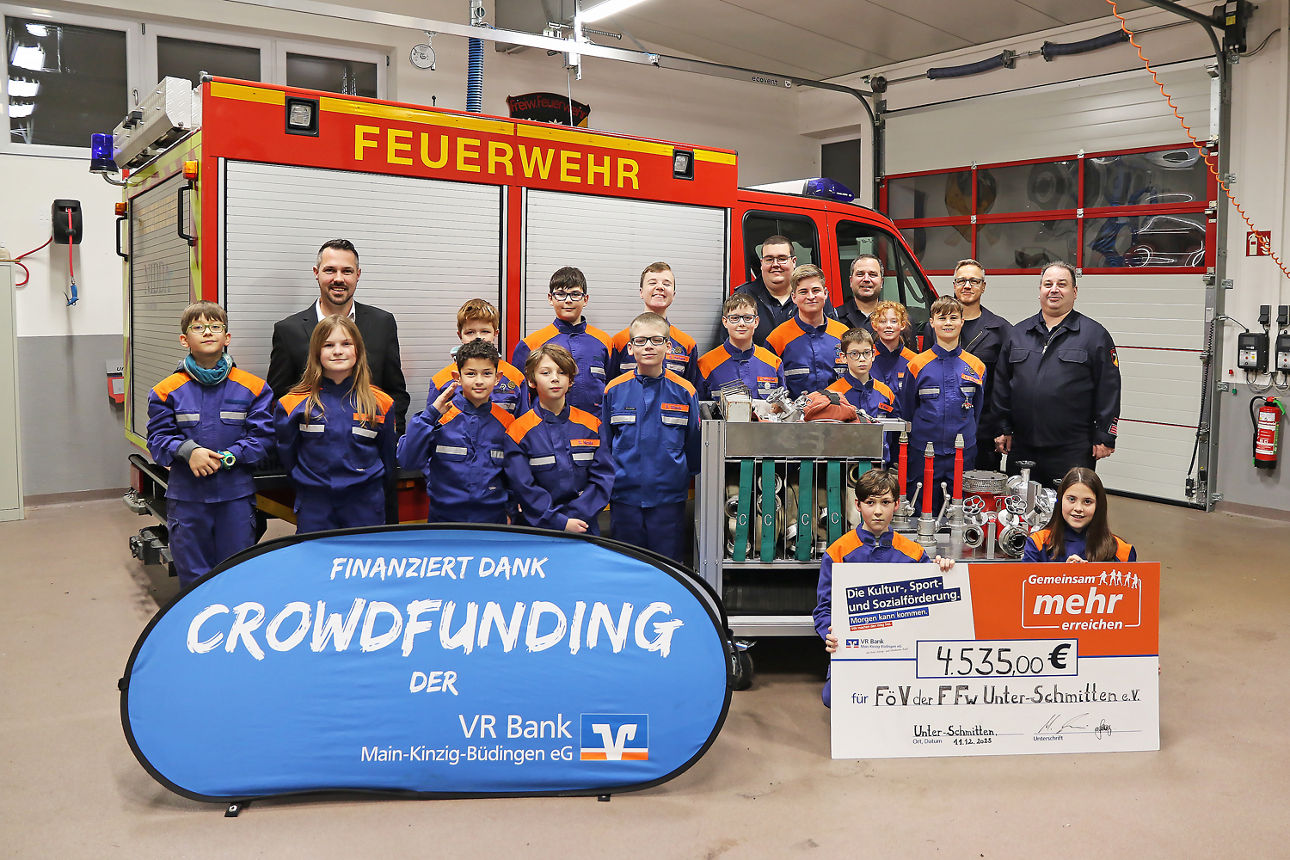 In einer Feuerwehrhalle steht eine Gruppe von rund 20 Feuerwehrangehörigen in Uniform vor ei