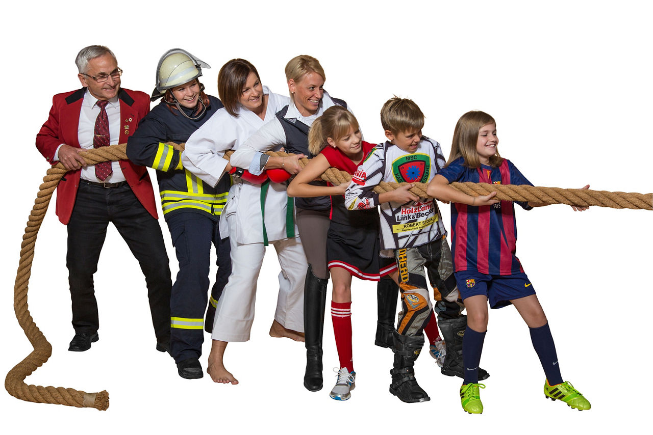 Vier Erwachsene und drei Kinder in Vereinskleidung ziehen an einem Tauseil.