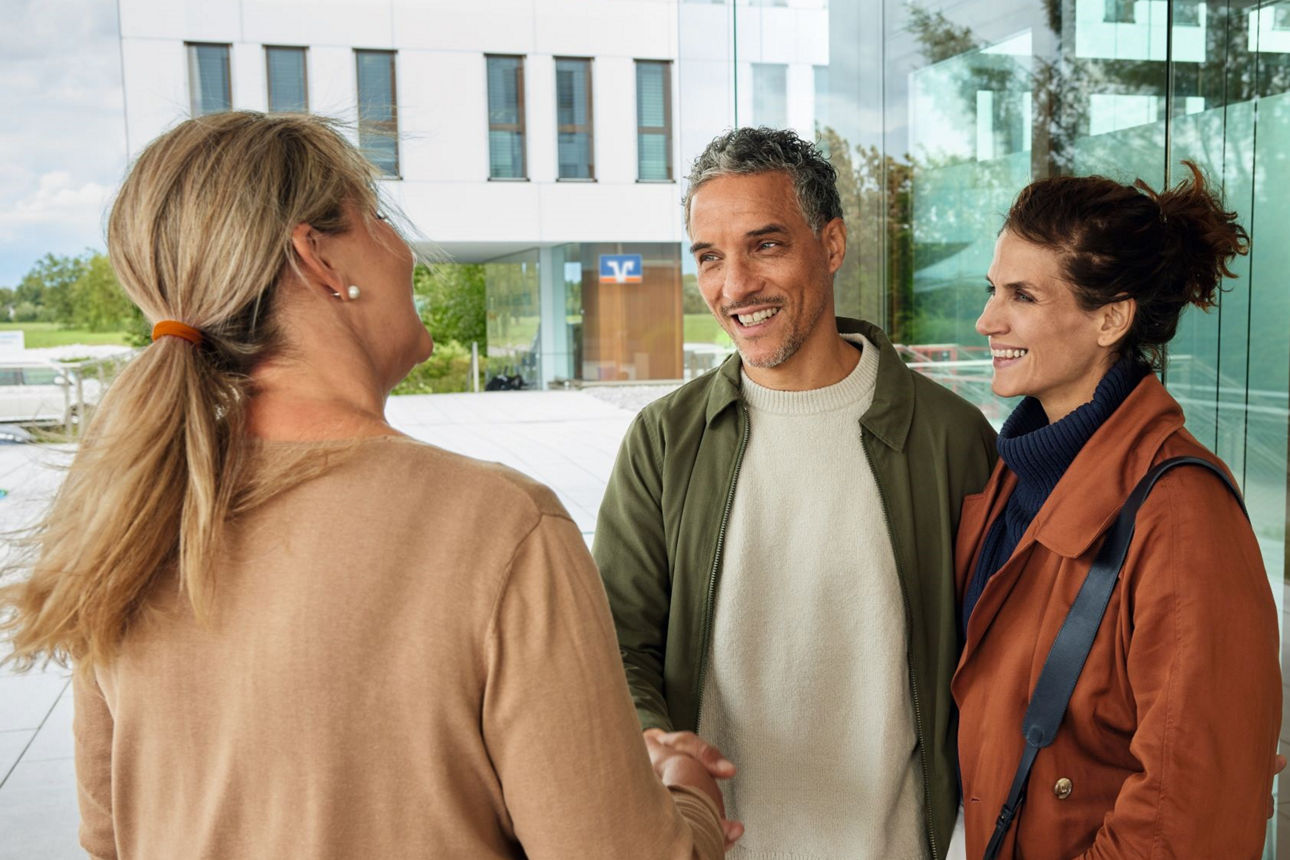 Eine Mitarbeiterin der Volksbank begrüßt ein Paar in der Bankfiliale