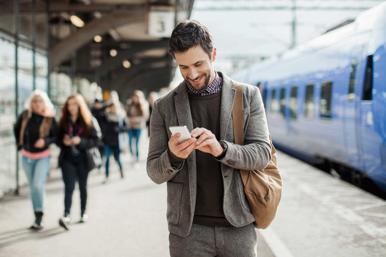 Mann schaut am Bahnhof auf sein Handy