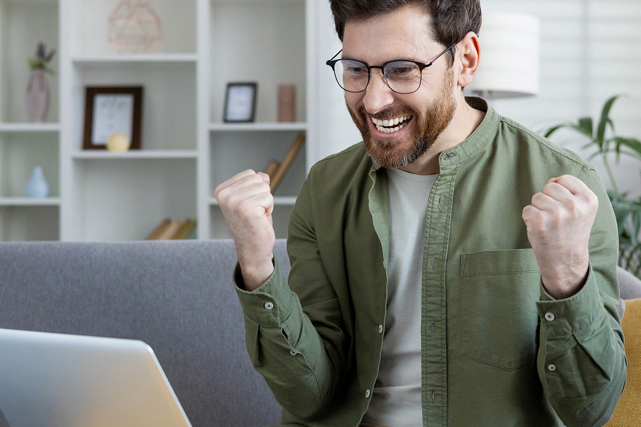 Ein Mann sitzt auf der Couch und jubelt vor dem Laptop