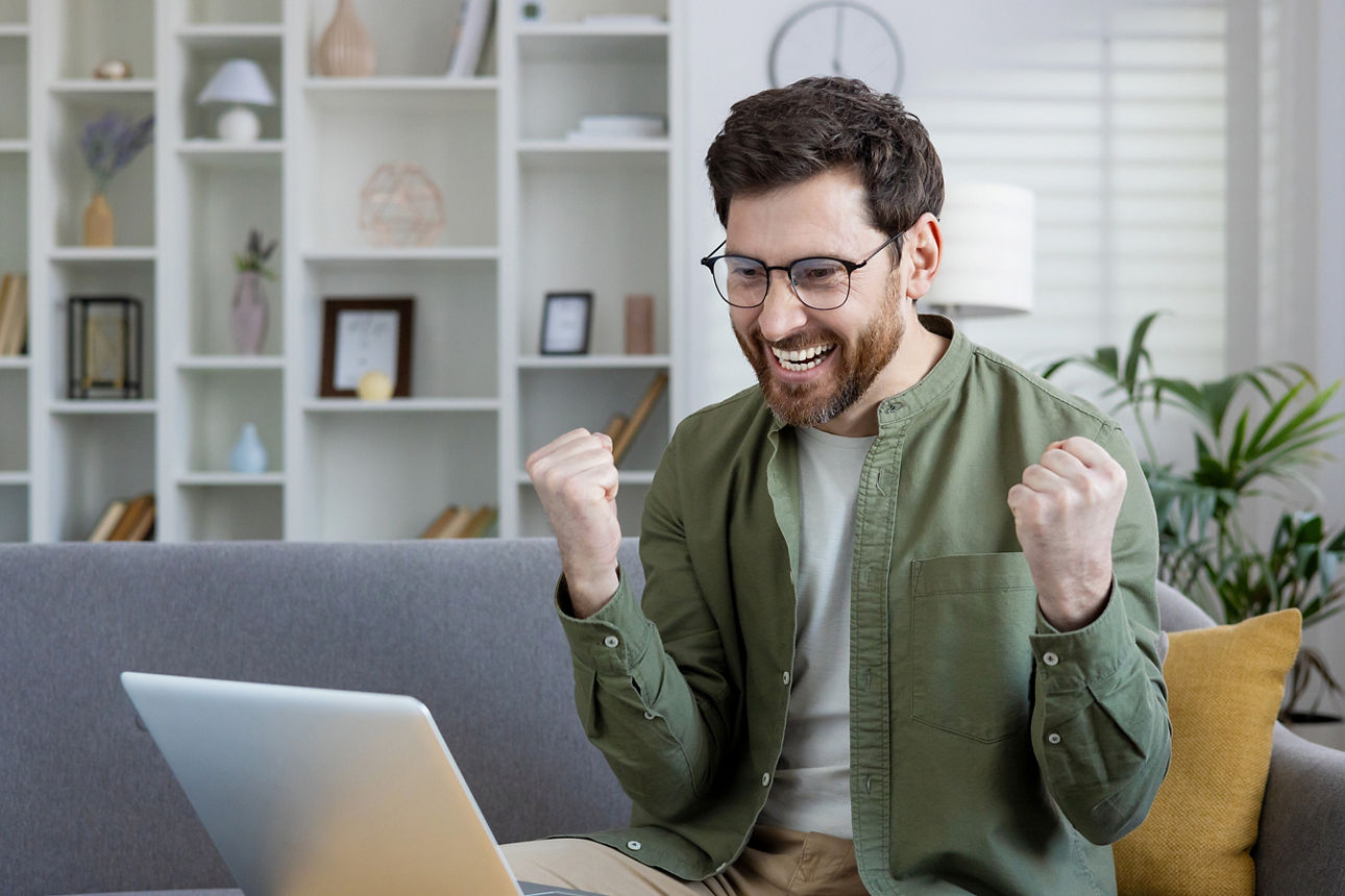 Ein Mann sitzt auf der Couch und jubelt vor dem Laptop