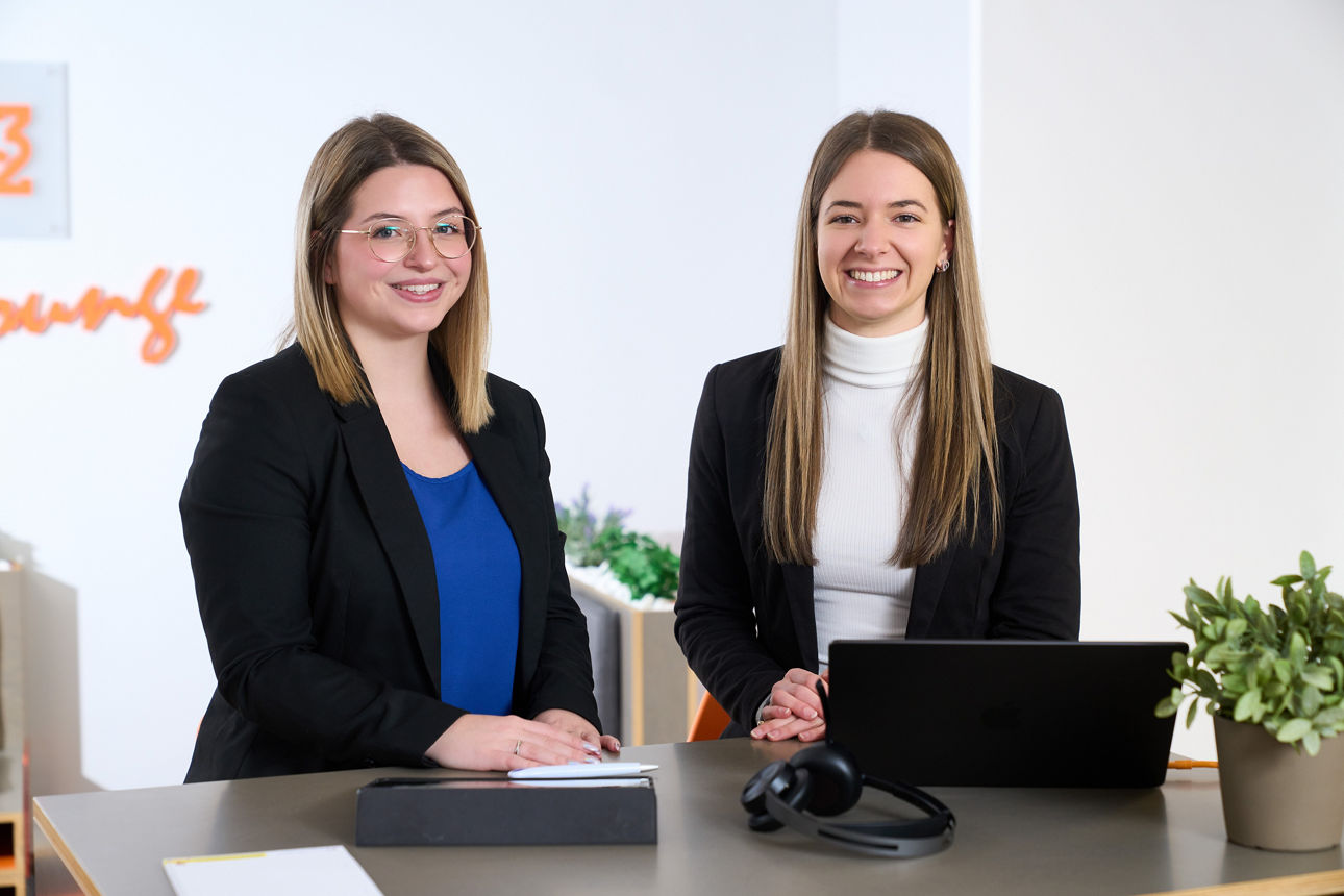 zwei Frauen stehen an einem Schreibtisch zusammen