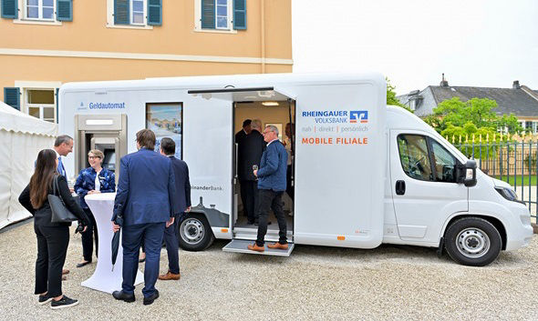 Das weiße Wohnmobil, welches zur Filiale auf Rädern umgebaut wurde, wird von den Vertretern rege begutachtet.