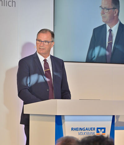 Herr Steinmacher steht am Rednerpult - er trägt einen Anzug und eine Krawatte mit Krawattennadel