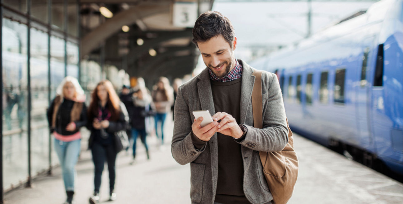 Mann mit Smartphone am Bahnsteig