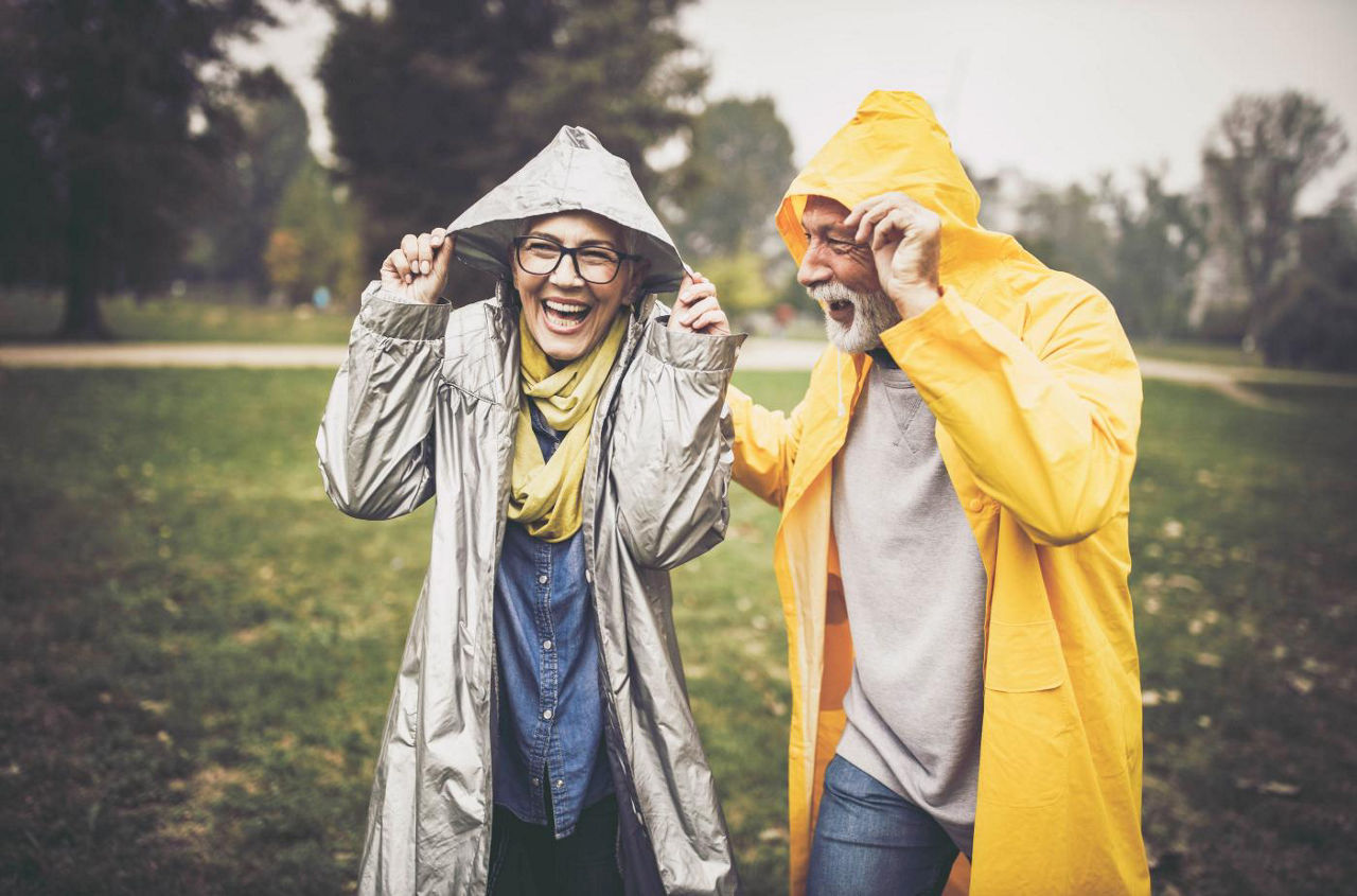 Älteres Paar im Regen mit Regenjacken und Kapuzen über dem Kopf