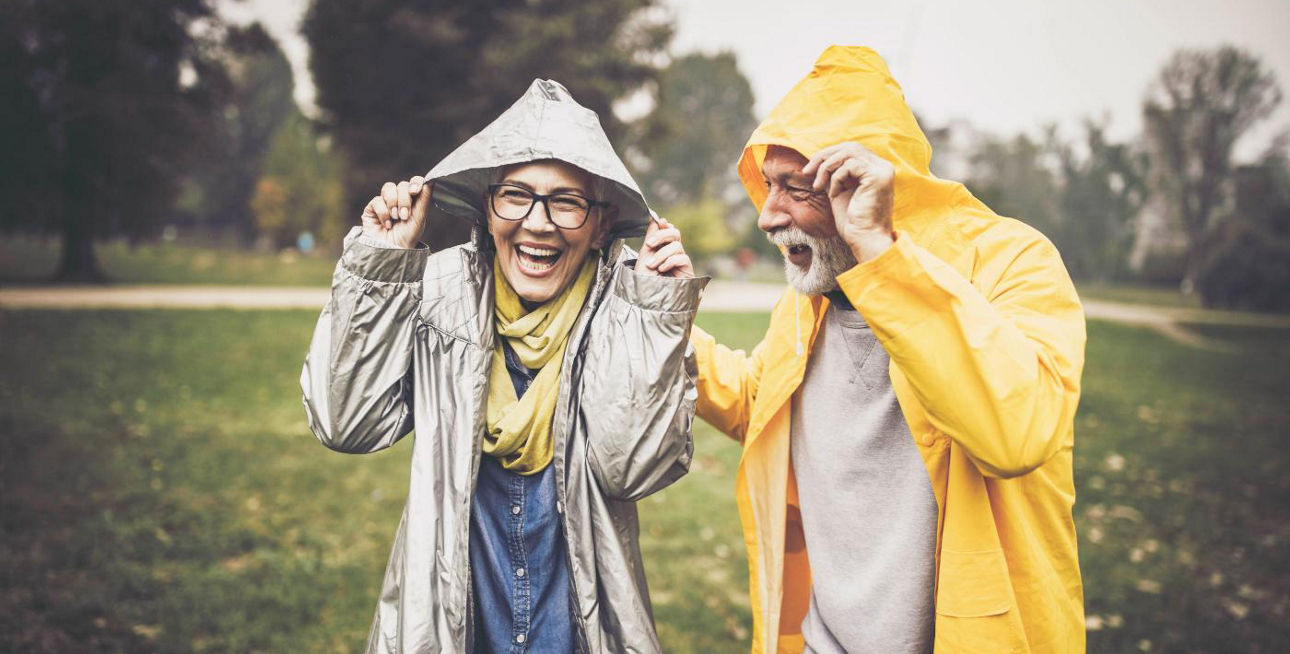 Älteres Paar im Regen mit Regenjacken und Kapuzen über dem Kopf