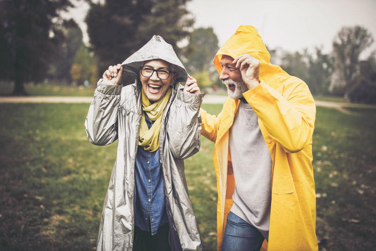 Älteres Paar im Regen mit Regenjacken und Kapuzen über dem Kopf
