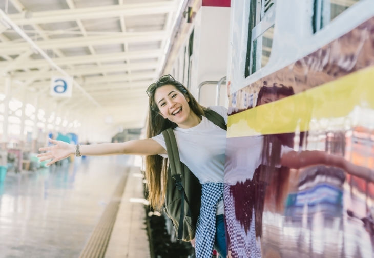 Junges Mädchen lehnt sich lächelnd auf dem Zug, welcher in einem Bahnhof steht und winkt