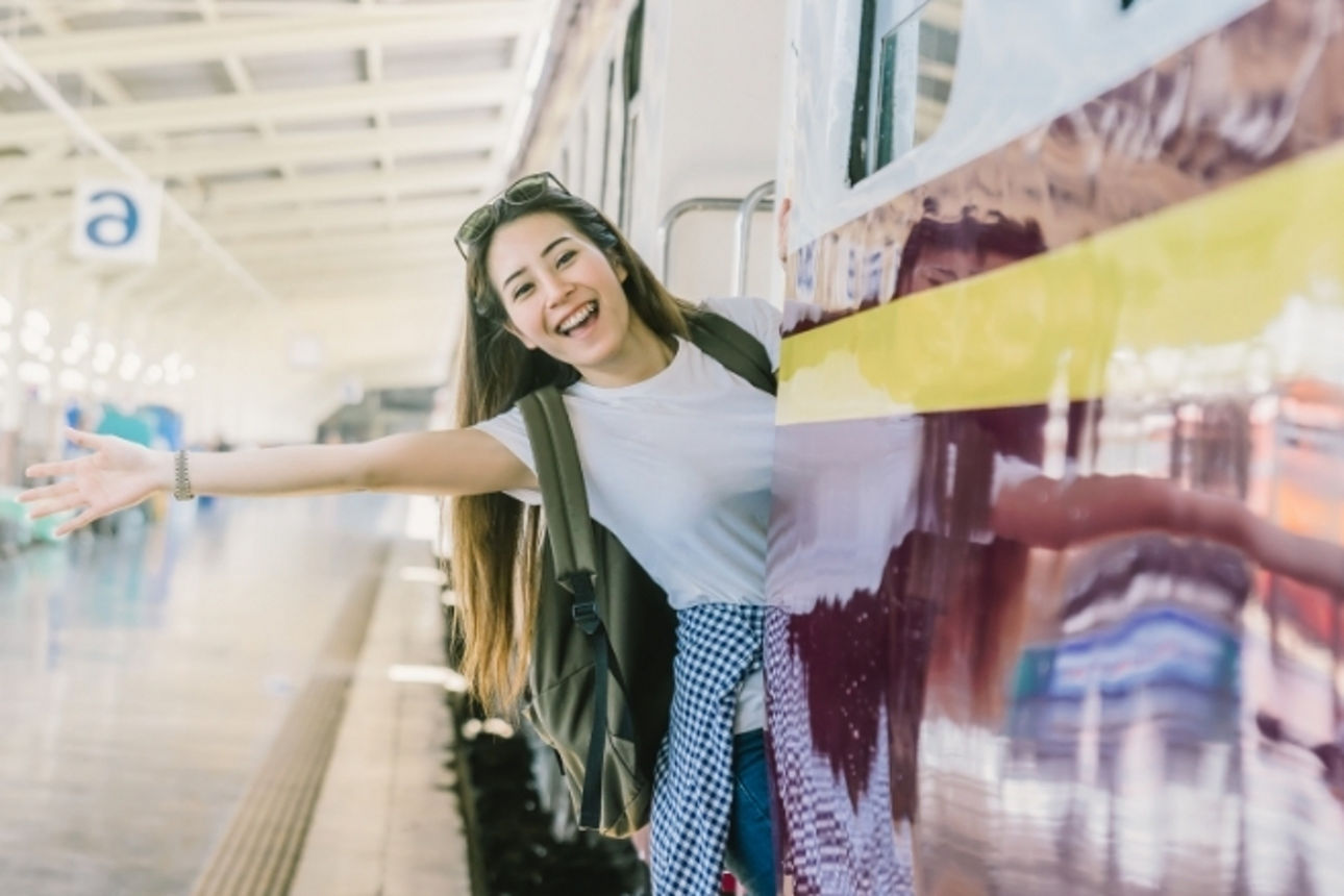 Junges Mädchen lehnt sich lächelnd auf dem Zug, welcher in einem Bahnhof steht und winkt