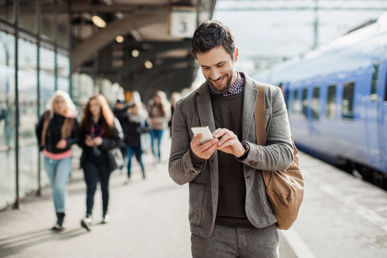 Ein Mann steht auf einem Bahnsteig und schaut lächelnd auf sein Handy