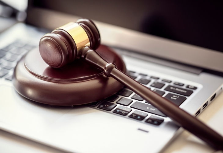 Brauner Holzhammer liegt mit der Unterlage auf einem silbernen Laptop
