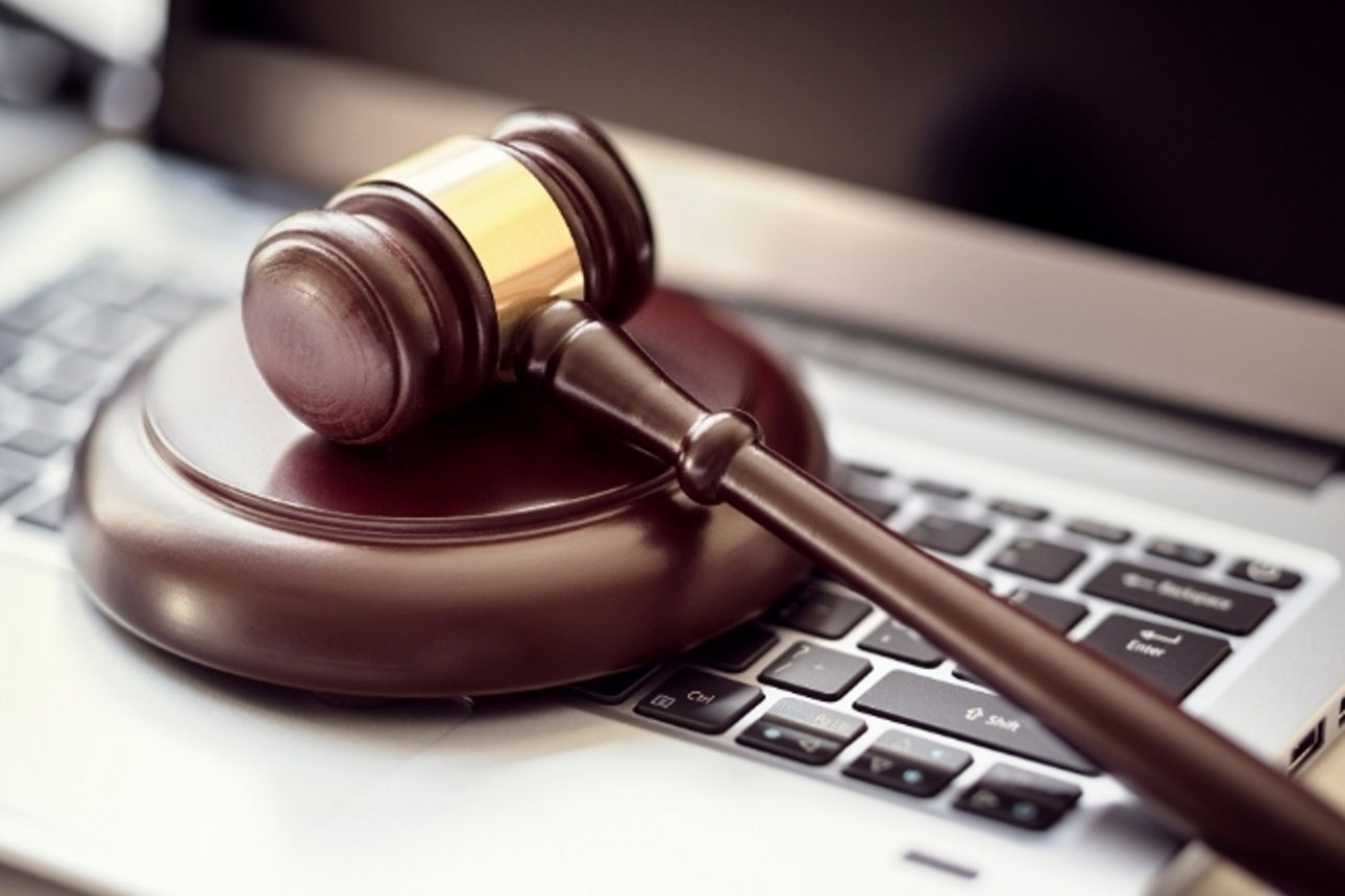 Brauner Holzhammer liegt mit der Unterlage auf einem silbernen Laptop