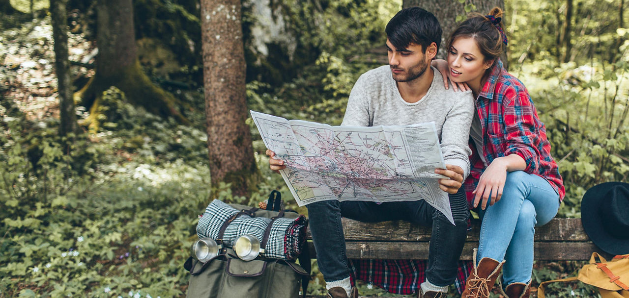 Ein Mann und eine Frau sitzen im Wald auf einer Bank und studieren eine Landkarte