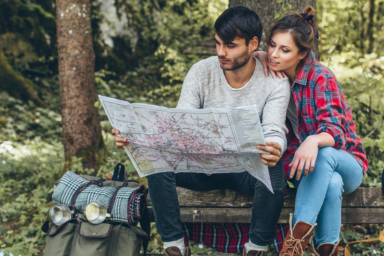 Ein Mann und eine Frau sitzen im Wald auf einer Bank und studieren eine Landkarte
