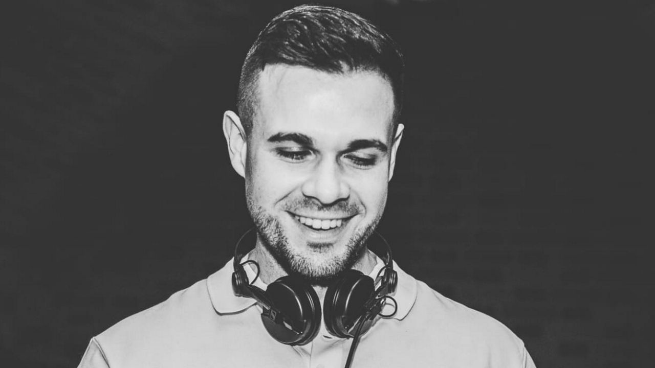 DJ Kaywe bei einem Auftritt, mit Kopfhörern um den Hals und konzentriert am DJ-Pult in einer Schwarz-Weiß-Aufnahme.