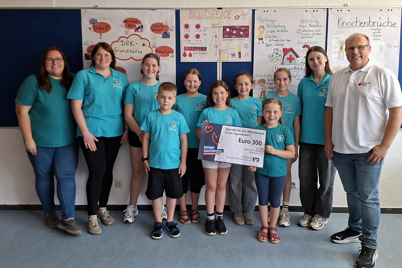 Eine Gruppe Kinder stehen vor einer Schultafel und halten einen Spendenscheck in der Hand.