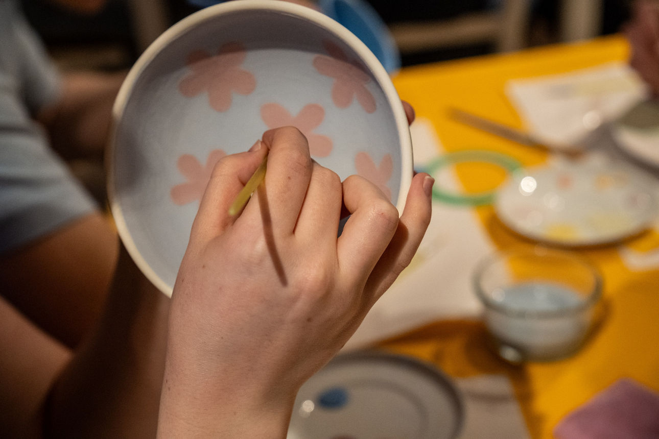 Eine Hand mit Pinsel bemalt einen Porzellanteller