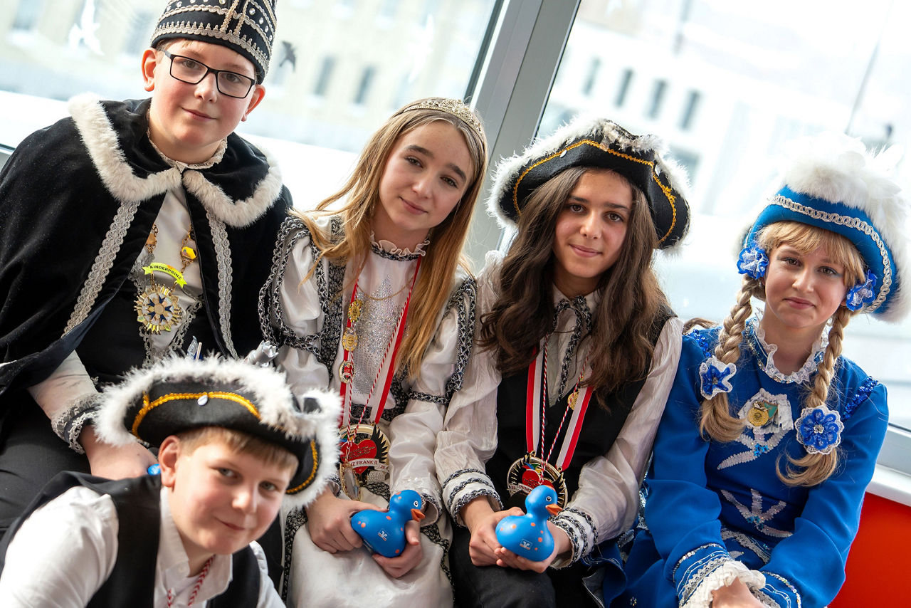 Fünf Kinder in traditionellen Karnevalskostümen (Garde und Piraten) sitzen nebeneinander und halten blaue Quietscheenten in d