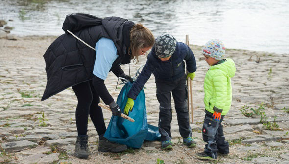 Mitarbeiterin der Rheingauer Volksbank eG und zwei Kinder räumen am Rhein auf.