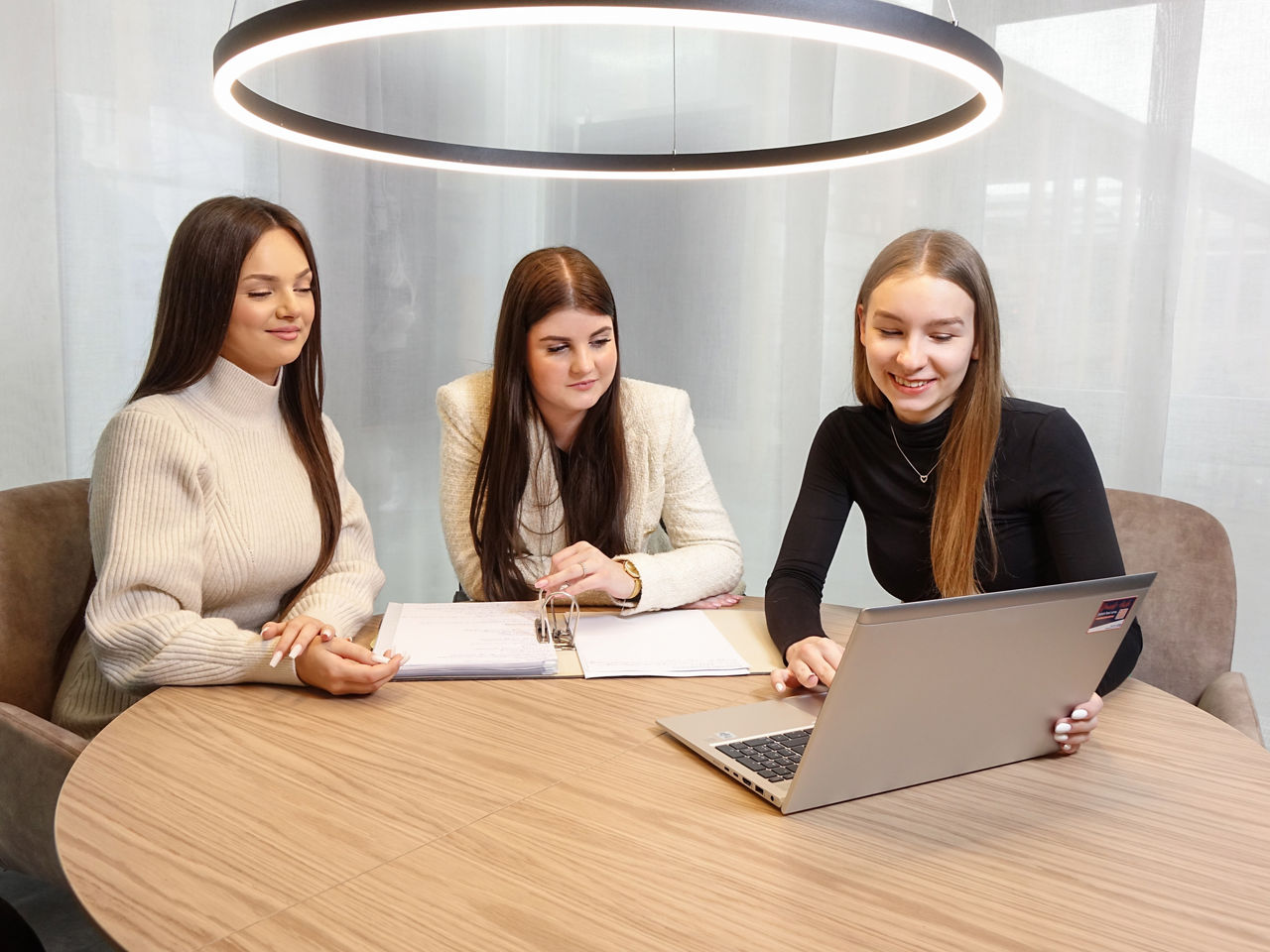 Drei junge Frauen sitzen am Tisch und arbeiten an einem Laptop