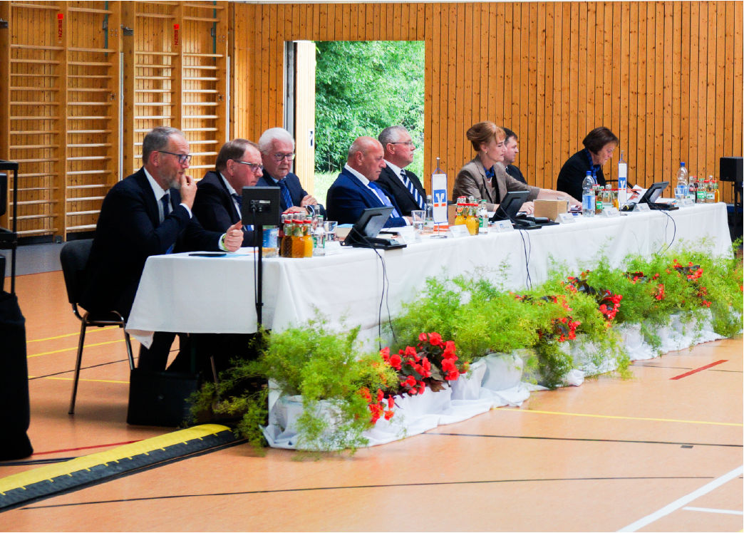 Viele Personen die an einem großen langen Tisch sitzen in einer Halle. 