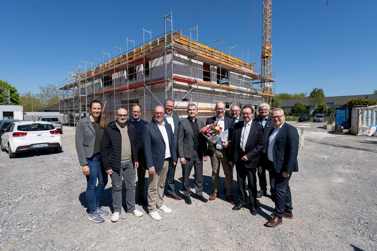 Auf dem Foto stehen zwölf Personen in einer Reihe vor dem Rohbau der Filiale Hardt.