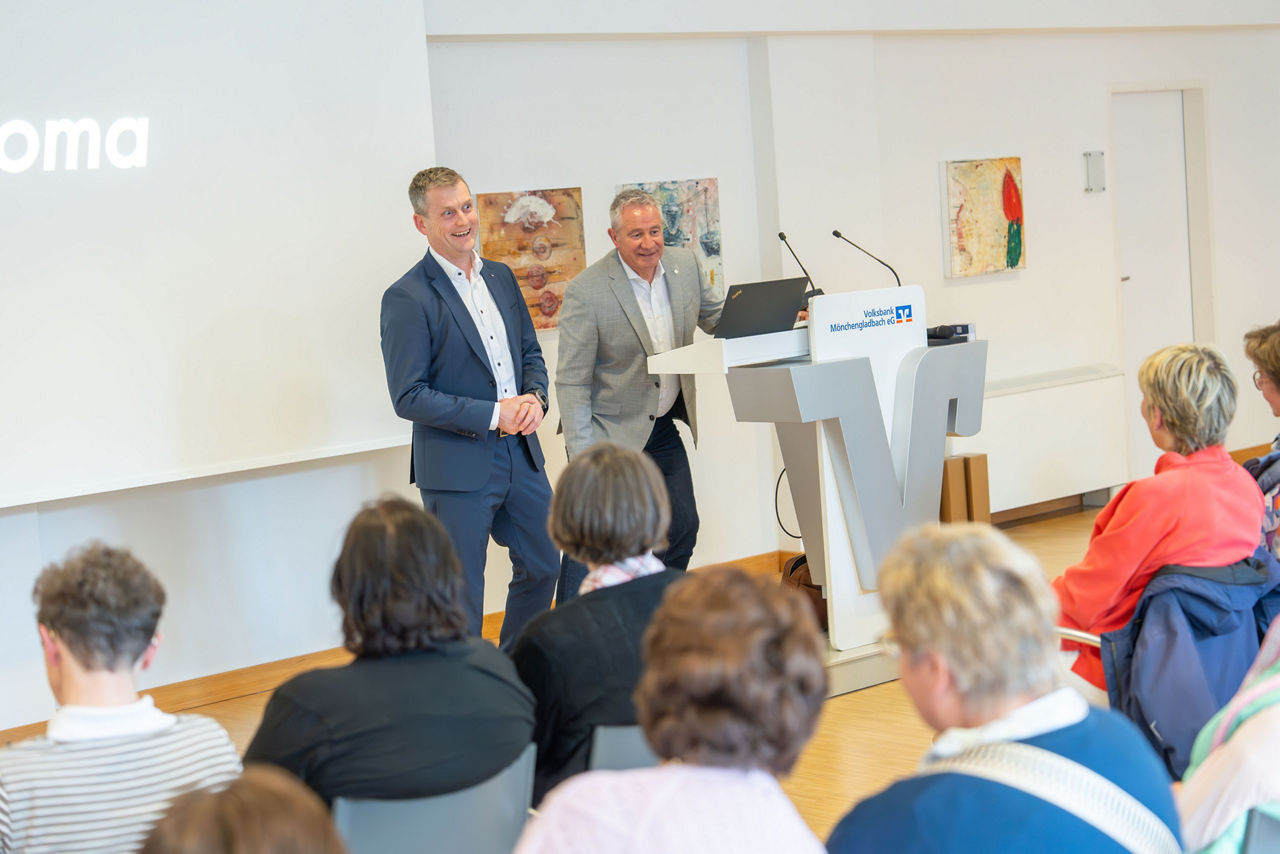 Sven Frauenkron und Edelbert Sangl von der Volksbank stehen am Rednerpult vor vielen sitzenden Frauen 