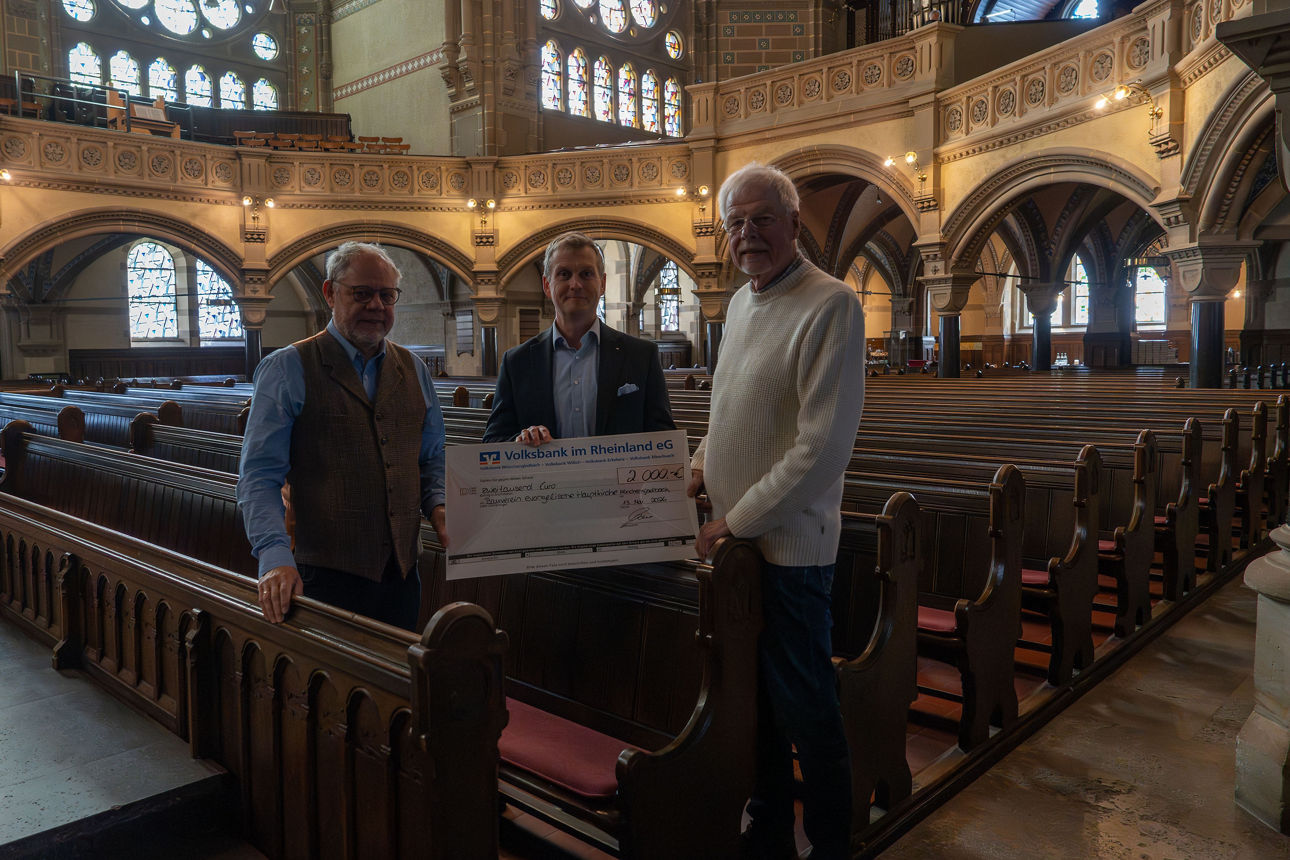 Auf dem Foto stehen drei Herren in einer Kirche und halten einen großen, symbolischen  Scheck in der Hand.