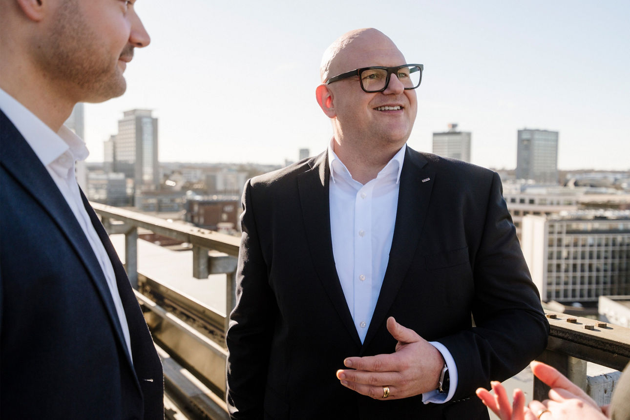 Zwei Männer im Gespräch auf der Dachterrasse eines hohen Gebäudes