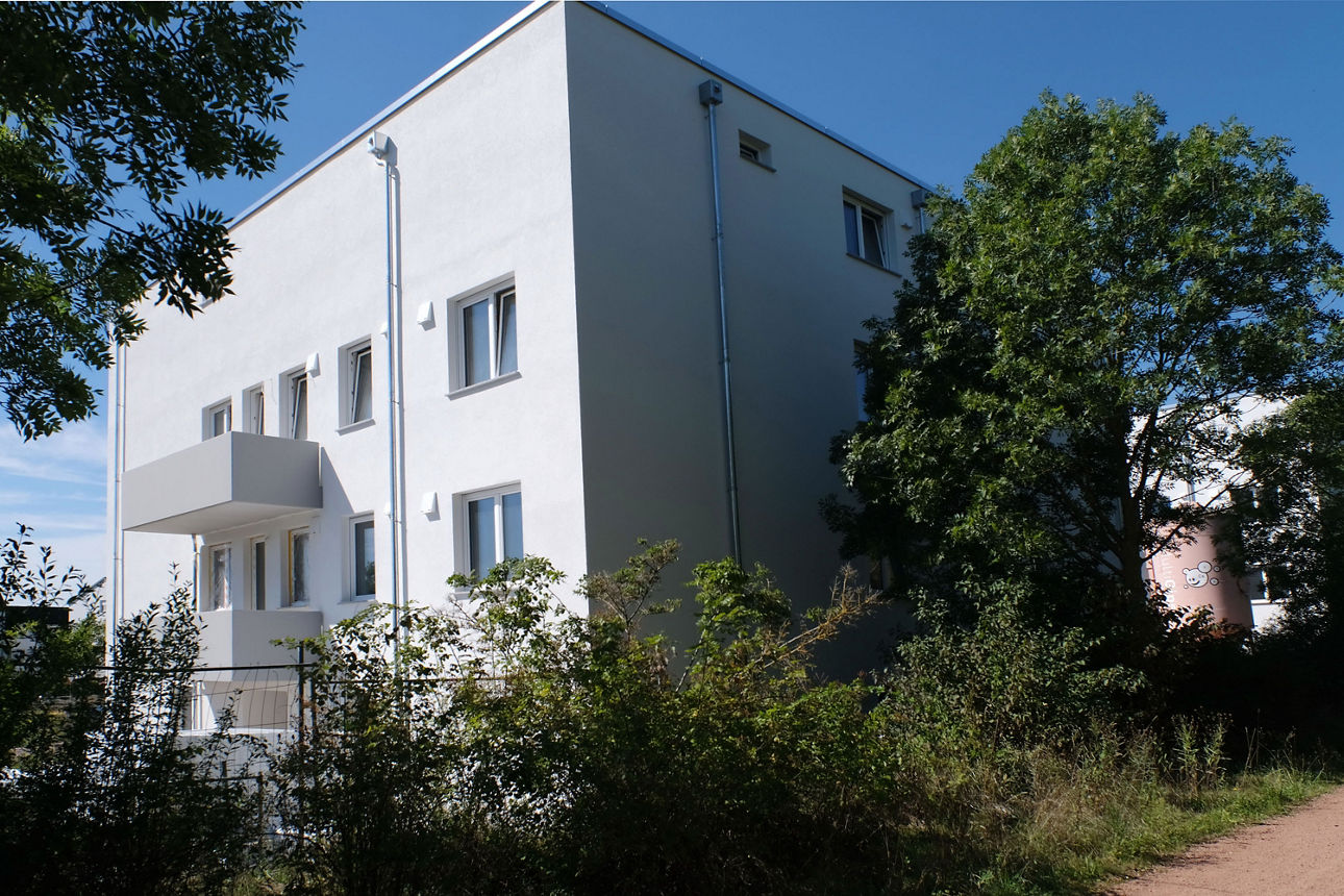 Moderne Wohnanlage mit Mehrfamilienhäusern, Balkonen und parkendem Auto in ruhiger Wohnstraße.
